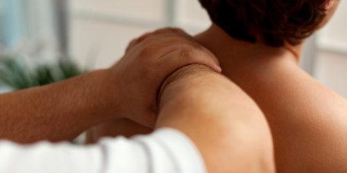 Inside, a massage therapist works on a man’s shoulders. The therapist is applying pressure, promoting relaxation and wellness through massage therapy techniques.